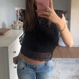 Svart spets topp från ONLY - Säljer en svart croppad topp från ONLY med vacker spets och detaljerade kanter. Toppen är ärmlös och har ett genombrutet spetsmönster både fram och bak. Perfekt för att lyfta en outfit med lite extra edge.