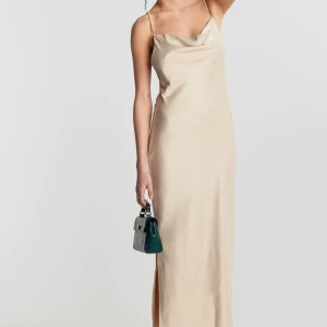 Beige långklänning med pärlband från Gina tricot  - Säljer en elegant beige långklänning från Gina tricot med pärlprydda axelband och draperad urringning. Klänningen har slits i sidan och är tillverkad i ett glansigt satinliknande material. Perfekt för speciella tillfällen.