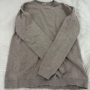 Beige stickad tröja - Mjuk och enkel beige stickad tröja med rund halsringning och långa ärmar. Tröjan har ribbade muddar vid ärmslut och nederkant, perfekt för lager-på-lager under kyligare dagar.