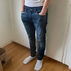Mörkblå jeans från Tiger Of Sweden - Säljer ett par mörkblå jeans med klassisk femficksdesign och normal passform. Jeansen har dragkedja och knapp framtill samt snygga slitningar för en avslappnad look. Midjemått 33 och längd 32, Modell, Evolve. 