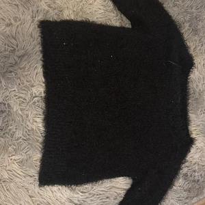 Svart fluffig tröja från Sinsay - Mysig svart fluffig tröja från Sinsay i storlek XS. Tröjan har lång ärm och är tillverkad i ett mjukt, lurvigt material som ger en cool och trendig look. Perfekt att styla med jeans eller kjol.