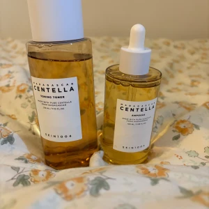 Centella toner och ampoule från SKIN1004 - Två produkter från SKIN1004: en toning toner i en rektangulär flaska med vitt lock och en ampoule i en rund flaska med pipett. Båda innehåller centella-extrakt och har en ljusgul färg. Perfekt för återfuktning och lugnande av huden.