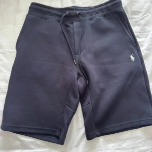 Mörkblå shorts från Polo Ralph Lauren - Snygga mörkblå shorts från Polo Ralph Lauren med dragsko i midjan och klassisk broderad logga på vänster ben. Mjukt material och två sidofickor. Perfekta för en avslappnad stil.
