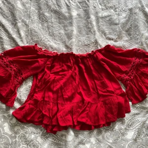 Röd offshoulder blus från FB Sister - Säljer en röd offshoulder blus från FB Sister i storlek XS. Blusen har vida ärmar med volangdetaljer och smock vid axlarna. Perfekt för dig som vill ha en färgstark och trendig topp med mycket volym och rörelse.
