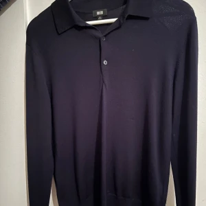 Svart långärmad pikétröja från Uniqlo - Säljer en stilren svart långärmad pikétröja från Uniqlo. Tröjan har klassisk krage och knäppning framtill med två knappar. Perfekt för en clean och enkel look.