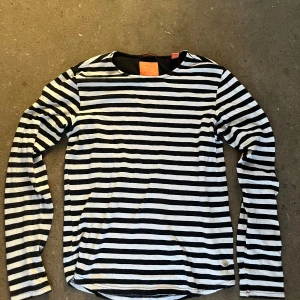  Scotch & Soda tröja  - Randig långärmad tröja från Scotch & Soda i svart och vitt. Klassisk passform med rund halsringning och mjukt bomullsmaterial. Perfekt för en avslappnad och stilren look. 