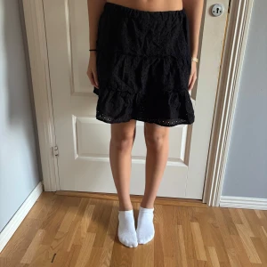 Svart volangkjol med broderade detaljer - Säljer en svart kortkjol med volanger och broderade detaljer. Kjolen har resår i midjan och är tillverkad i ett lätt tyg som ger en luftig känsla. Perfekt att styla med en enkel topp eller hoodie. Den är i storlek m men är ganska stor i storlek den är i från new yorker.