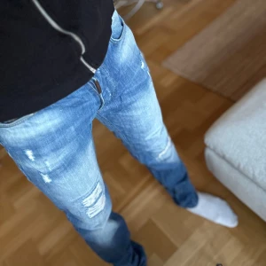 Blå slitna jeans från Adrian Hammond - Säljer ett par blå jeans från Adrian Hammond med slitningar och distressed detaljer på både fram- och baksida.