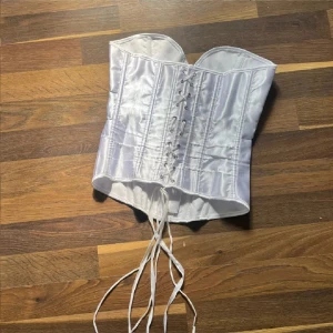 Vit korsett med snörning(lite små fleckar men de syns inte) bilderna är inte mina men skriv om ni vill ha bilder hur den sitter 💞 - Snygg vit korsett med snörning bak och knäppning fram. Gjord i glansigt material med markerade sömmar för en stilren look. Perfekt att styla till olika outfits.