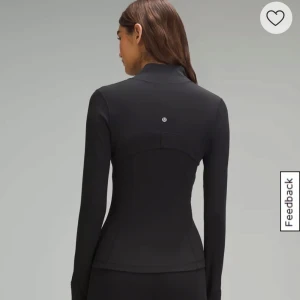 Svart träningsjacka från Lululemon - Snygg svart träningsjacka från Lululemon med figurnära passform och hel dragkedja framtill. Jackan har lång ärm och hög krage, perfekt för träning eller som ett extra lager. Diskret logga på ryggen.