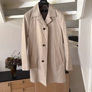 Beige Boss rock size 48 - Stilren och knappt använd beige rock från BOSS med klassisk krage och tre knappar framtill. Jackan har två sidofickor och två innerfickor. Perfekt för vår och höst.  Storlek 48. 