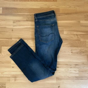 Mörkblå jeansbyxor från Jack & Jones - Säljer ett par mörkblå jeans från Jack & Jones med klassisk femficksdesign och snygga slitningar framtill. Jeansen har normal passform och raka ben. Perfekta till vardags för en stilren look.