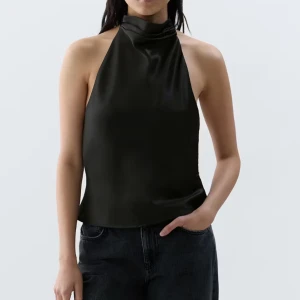 Svart halterneck topp - Säljer en svart halterneck topp med hög krage och öppen rygg. Toppen har en elegant och stilren design som passar perfekt till både jeans och kjol. Materialet är mjukt och har ett lätt glansigt utseende.