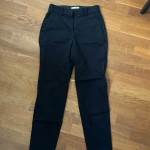 Svarta kostymbyxor från H&M - Klassiska svarta kostymbyxor från H&M med raka ben och bälteshällor. Byxorna har dragkedja och hyska fram samt två fickor bak. Perfekta för en stilren look.