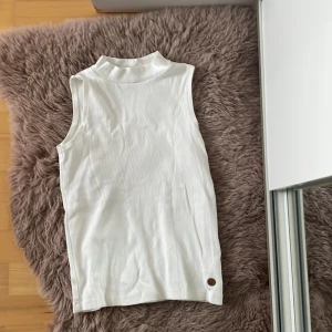 Vit ribbad ärmlös polotopp - Säljer en vit fin  ribbad ärmlös polotopp med hög hals. Toppen har en enkel och stilren design, perfekt att matcha med olika outfits. Superskön och lätt att bära.storlek 146/152 från Kappahl.hör av dig om du har frågor eller funderingar 💕