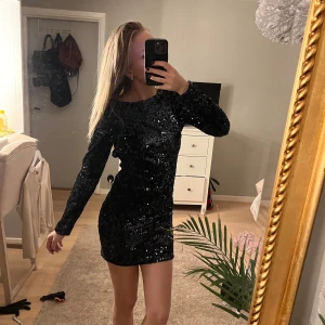Svart glittrig klänning - Snygg mörkblå glittrig klänning med lång ärm och en öppen rygg. Perfekt för en kväll ute eller nyår. Klänningen har en tight passform som framhäver figuren.