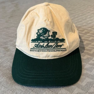 Vit och mörkgrön keps från Aime Leon Dore - Snygg och stilren keps i vit och mörkgrön färg från Aime Leon Dore med broderad logga och text framtill. Kepsen har klassisk form med böjd skärm. Helt oanvänd. 