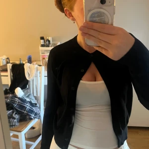 Svart kofta från H&M - Säljer en klassisk svart kofta från H&M i storlek XS. Koftan har rund halsringning, långa ärmar och knäppning framtill med svarta knappar. Perfekt att slänga över en topp eller klänning. Hör av er vid frågor eller bilder.💛