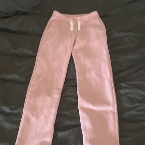 Rosa mjukisbyxor från russemerch - Säljer ett par ljusrosa mjukisbyxor från Russemerch i storlek XS. Byxorna har resår i midjan med vit snören och är tillverkade i ett mjukt och fleeceliknande material på insidan. Perfekta för en avslappnad stil. Endast använda ett fåtal gånger, inga defekter.