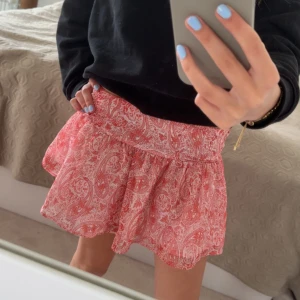 Rosa paisleymönstrad kortkjol - Supersöt kortkjol i rosa med vitt paisleymönster. Kjolen har volang och bred linning som ger en skön passform. Perfekt för varma dagar och enkel att matcha med olika toppar. Sparsamt använd 