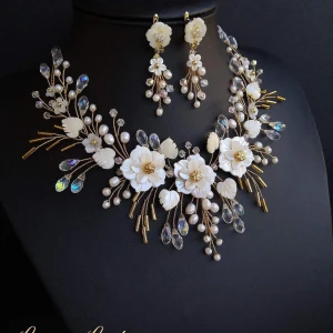 Brudhuvudbonad och örhängen – Handgjorda med naturliga snäckskal och kristaller - Unikt halsband och matchande örhängen med vita blommor, pärlor och gnistrande kristaller. Blommorna har gulddetaljer och halsbandet har en elegant, grenliknande design. Perfekt för speciella tillfällen.