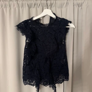 Mörkblå spetsblus från Zara - Säljer en mörkblå ärmlös blus från Zara i vacker spets. Blusen har fina spetsdetaljer längs kanterna och en feminin, elegant look. Perfekt att styla med både jeans och kjol för en trendig outfit.