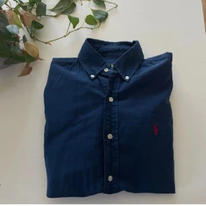 Mörkblå skjorta från Ralph Lauren - Klassisk mörkblå skjorta från Ralph Lauren med button-down krage och vita knappar. Ikonisk röd broderad logga på bröstet. Strorlek: Xs men sitter mer som S. Mvh Emil