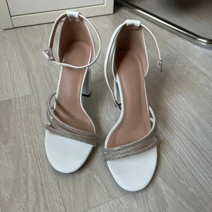 Klackarskor  - Säljer ett par vita klackar med glittrande detaljer och en justerbar rem runt vristen. 