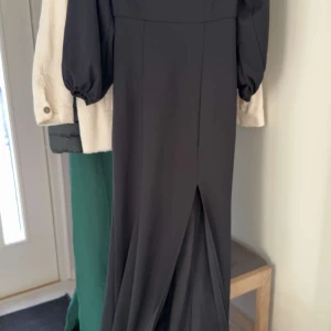 Svart långklänning med puffärmar från Bubbleroom - Säljer en elegant svart långklänning från Bubbleroom med puffiga långa ärmar och en snygg slits framtill. Klänningen har en figurnära passform och dragkedja i ryggen. Perfekt för speciella tillfällen!