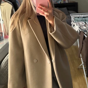 Beige kappa med klassisk krage - Säljer en stilren beige kappa med klassisk krage och två knappar framtill. Jackan har lång ärm och rak passform som ger en snygg och tidlös look. Perfekt för dig som vill ha en enkel men elegant jacka till garderoben.