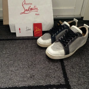 Christian Louboutin  - Snygga sneakers från Christian Louboutin med vit skinnpanel, grå textil och mörkblå detaljer. Klassisk rund tå, svarta skosnören och platt sula. Perfekt för dig som vill ha en exklusiv och stilren look med en lyxig touch. Dom har lite små skavanker här och där men båda skorna är hela🙌🙌🤝💠