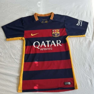 FC Barcelona Neymar Jr 11 matchtröja Nike - Barça 2015/16 hemmafotbollströja med Neymar Jr 11 på ryggen. Klassiska breda blå och röda ränder, gula detaljer och klubbmärke på bröstet. Tillverkad i Dri-FIT-material för bästa komfort. Snygg gulrandig krage och sponsorer tryckta på framsidan.