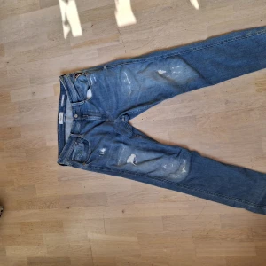 Replay Anbass blå jeans herr 32/30 - Säljer ett par Replay Anbass jeans i klassisk blå tvätt med slitna detaljer och snygga slitningar på benen. Modellen har normal passform och raka ben. Perfekta för dig som gillar en avslappnad men trendig look. Materialet är mjukt jeans i bomull.
