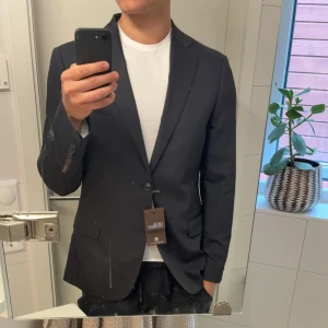 Svart kavaj från Oscar Jacobson - Helt oanvänd svart kavaj från Oscar Jacobson!🥃 Klassisk passform och snygga detaljer som två framfickor med lock och en bröstficka. Kavajen har enkla knappar framtill och är tillverkad i ett mjukt material som ger en exklusiv känsla.