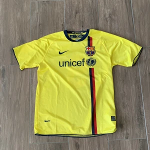 Barcelona Ibrahimović bortatröja Nike - Gul FC Barcelona bortatröja med Ibrahimović och nummer 9 på ryggen. Nike Dri-FIT material, kortärmad med blå och röd rand på framsidan, klubbmärke och Unicef-tryck. Champions League-märke på ärmen och blå detaljer vid krage och ärmslut.
