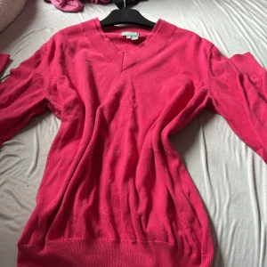 Rosa v-ringad tröja från Lyle & Scott - Snygg rosa tröja från Lyle & Scott i mjuk bomull. V-ringad halsringning och långa ärmar ger en klassisk look. Perfekt att matcha med jeans eller kjol för en chill och stilren vibe.