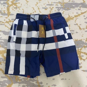 BURBURRY  - Snygga shorts med stora blå, vita och svarta rutor samt en röd rand. De har elastisk midja med svart snörning och praktiska fickor på sidorna. Perfekta för sommaren när du vill sticka ut lite extra.