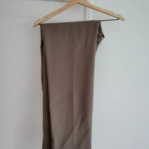  Filippa K Relaxed Wool trousers - Stilrena beige kostymbyxor från Filippa K med elastisk midja och raka ben. Byxorna har diskreta fickor och är tillverkade i ett mjukt material som ger en clean och modern look. Perfekta för dig som gillar minimalistisk stil.