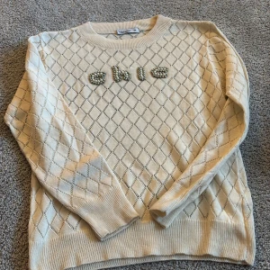 Beige stickad tröja med pärldetaljer - Supersöt beige stickad tröja från Fullamoda med rutigt hålmönster och texten 'chic' i pärlor. 