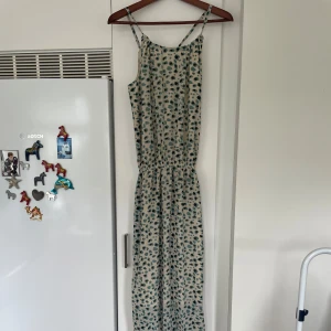 Mönstrad långklänning från Femme Collection - Långklänning med smala axelband och fickor. Klänningen har ett lekfullt mönster i blått och svart på beige botten, resår i midjan och ledig passform. Perfekt för sommarens varma dagar och har en luftig känsla.