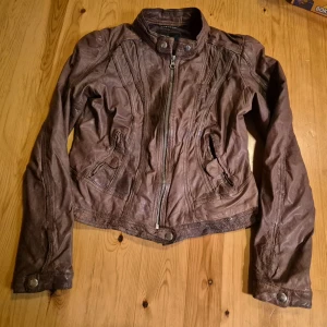 Brun skinnjacka från Rock'n Blue strlk 40 - Snygg brun skinnjacka från Rock'n Blue i äkta läder. Jackan har coola detaljer med dragkedja framtill, ståkrage med tryckknapp och fickor med lock. Perfekt för dig som vill ha en tidlös och edgy look. Fodret är i bomull och polyester. Använd fåtal gånger.