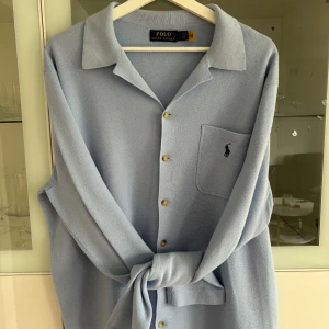 Ljusblå skjorta från Polo Ralph Lauren - Snygg ljusblå skjorta från Polo Ralph Lauren med klassisk krage, guldiga knappar och bröstficka med broderad logga. Skjortan är långärmad och har en relaxed fit, perfekt för en chill och stilren look.