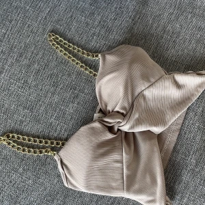 Beige ribbad linnetopp med guldkedjor - Supersnygg beige ribbad linnetopp från New Collection med trendiga axelband i guldfärgad kedja. Toppen har en knutdetalj framtill som ger en cool och unik look. Perfekt för dig som vill sticka ut och addera lite edge till outfiten.