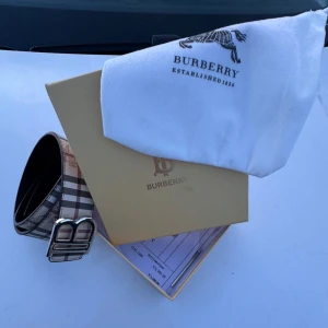 Rutig Burberry bälte med silverdetaljer - Helt oanvänd och snygg Burberry bälte med klassiskt rutigt mönster i beige, svart, rött och vitt. Bältet har en stilren silverfärgad spänne med Burberrys ikoniska B-logga. Kommer med originalförpackning, dustbag och påse. Perfekt accessoar för att lyfta din outfit.
