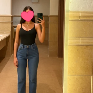 Svart ribbad bodysuit med smala axelband - Svart bodysuit med smala justerbara axelband och v-ringad halsringning. Tillverkad i ribbad stretchig syntet som formar kroppen. Perfekt att styla med jeans eller kjol.