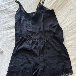 Svart pyjamas med spets från H&M - Svart pyjamas från H&M med tunna axelband och v-ringning dekorerad med blommig spets. Toppen är i mjukt material och har en elegant, feminin känsla. Perfekt att styla lager på lager eller som den är för en chic look.