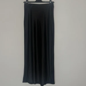 Svart satinkjol från Zara XS - Helt ny snygg svart långkjol från Zara i glansigt satinmaterial. Kjolen har en rak och stilren passform som faller snyggt längs kroppen. Perfekt för dig som gillar minimalistisk och trendig stil. Och perfekt nu till sommaren. Ändast testad aldrig använd, tyvärr är den för liten för mig och kan därför inte använda den, den är köpt i Spanien för 25,95 euro priset motsvarar 292 kr 🍀🩷
