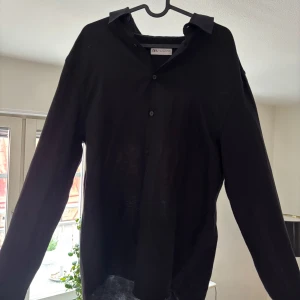Svart linneskjorta från Zara - Svart skjorta från Zara i luftig linnekvalitet. Klassisk krage, knäppning framtill och långa ärmar. Skjortan har en avslappnad passform och är perfekt för en stilren look. Stryks till innan den skickas!