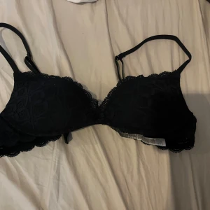 Svart spetsig korsett-bh 70B - Säljer en svart korsett-inspirerad bh med vacker spets och justerbara axelband. Bh:n har fina spetsdetaljer längs kanterna och lätt vadderade kupor för extra form. Perfekt för dig som gillar en feminin och stilren look.