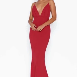 Röd långklänning med djup v-ringning - Supersnygg röd långklänning med smala axelband och djup v-ringning framtill. Klänningen har en figurnära passform och öppen rygg som ger en elegant och modern look. Perfekt för bal eller festliga tillfällen
